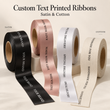 Load image into Gallery viewer, Four rolls of printed ribbon in black, blush pink, white, and cream are displayed on a light beige background. The top text reads 'Custom Text Printed Ribbons' with 'Satin &amp; Cotton' below.
